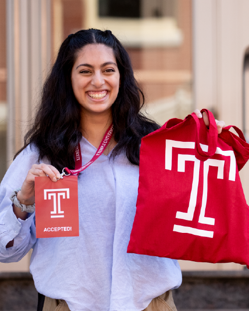 a student holding a card and a swag bag with Temple logos on them
