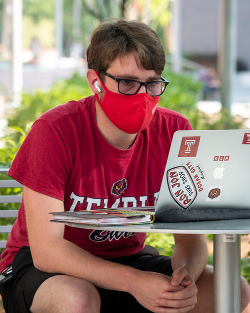 a Temple student studying in his laptop outdoors